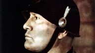 Dieses Porträt von Benito Mussolini zeigt den Diktator in militärischer Uniform mit Helm. Er blickt starr zur Seite.