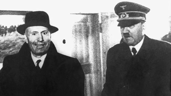 Das Bild zeigt Mussolini in Mantel und Hut gemeinsam mit Hitler in Uniform. Mussolini lächelt erleichtert über seine Befreiung.