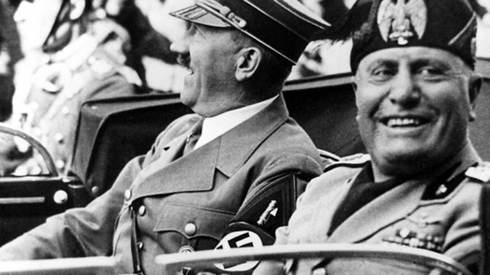 Das Bild zeigt Hitler und Mussolini in einem offenen Wagen fahrend. Beide Diktatoren scheinen sich zu amüsieren.
