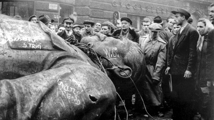 Schwarzweiß-Foto: Ein Stalin-Denkmal liegt auf der Straße, umringt von Schaulustigen
