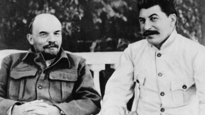 Schwarzweiß-Foto: Lenin und Josef Stalin sitzen auf Stühlen und lächeln in die Kamera