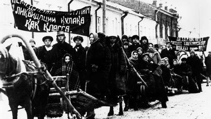 Schwarzweiß-Foto der Deportation von Kulaken: Ein langer Menschenzug auf Schlitten, die von Pferden gezogen werden.