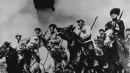 Schwarzweiß-Foto: Eine Abteilung der legendären Ersten Reiterarmee im russischen Bürgerkrieg, berittene Soldaten auf ihren Pferden mit wehender Fahne.