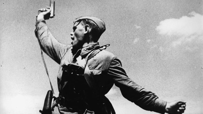Schwarzweiß-Foto: Soldat mit hochgestreckter Pistole.