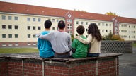 Eine Familie sitzt Arm in Arm vor einem Asylbewerberheim.
