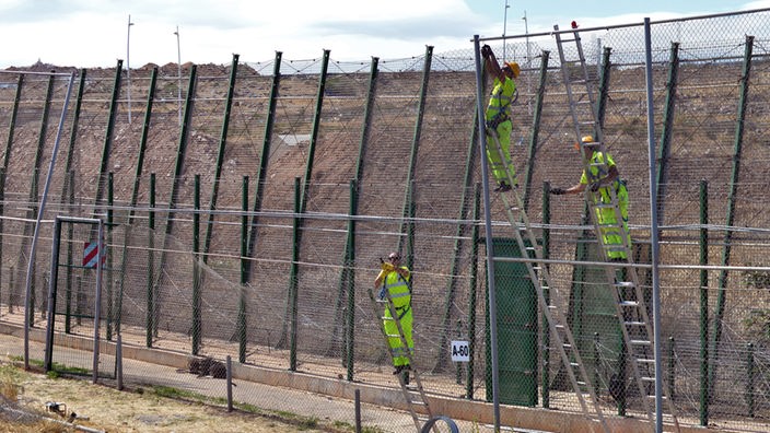 Arbeiter errichten eine Art Bollwerk an einer Grenze, um Fluchtwege zu schließen.