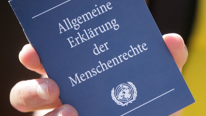 Eine Hand hält ein kleines Heft mit dem Titel "Allgemeine Erklärung der Menschenrechte hoch". | Bildquelle: dpa Eine Hand hält ein kleines Heft mit dem Titel "Allgemeine Erklärung der Menschenrechte hoch".