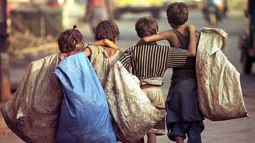 Vier Kinder gehen barfüßig nebeneinander. Sie tragen große Müllsäcke.
