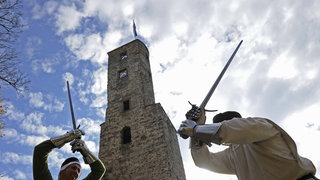 Zwei Ritter duellieren sich vor einer Burg.