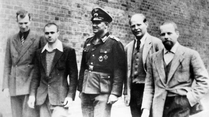 Schwarzweiß-Aufnahme: Bonhoeffer (Zweiter von rechts) und drei Mitinsassen laufen über den Gefängnishof in Berlin-Tegel. In der Mitte in Uniform: Oberfeldwebel Napp, der die Fotoaufnahme veranlasst hat.