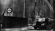 Schwarzweiß-Foto: Feuerwehrauto vor einer brennenden Synagoge.