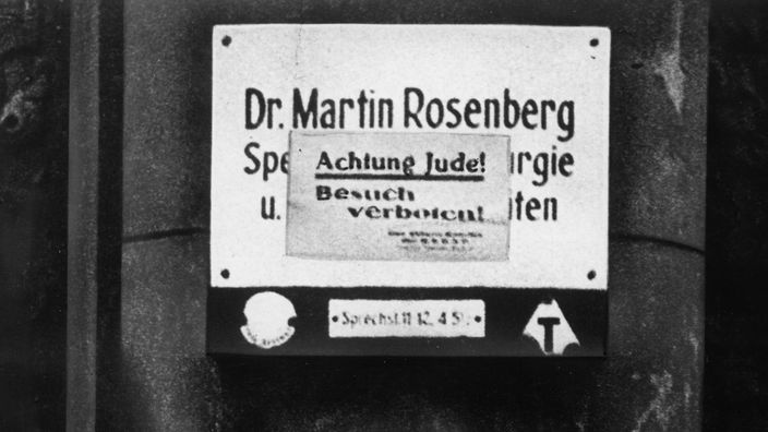 Schwarzweiß-Bild: Ein Schild 'Achtung Jude! - Besuch verboten!' befindet sich an der Tür einer jüdischen Arztpraxis.