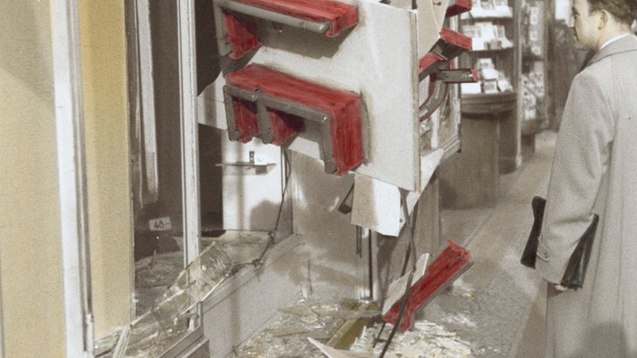 Schwarzweiß-Bild: Ein Mann steht vor einem zerbrochenen Schaufenster. | Bildquelle: akg Schwarzweiß-Bild: Ein Mann steht vor einem zerbrochenen Schaufenster.