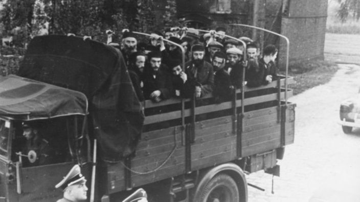 Schwarzweiß-Bild: Ein Lastwagen, auf dem jüdische Männer sitzen, fährt davon.