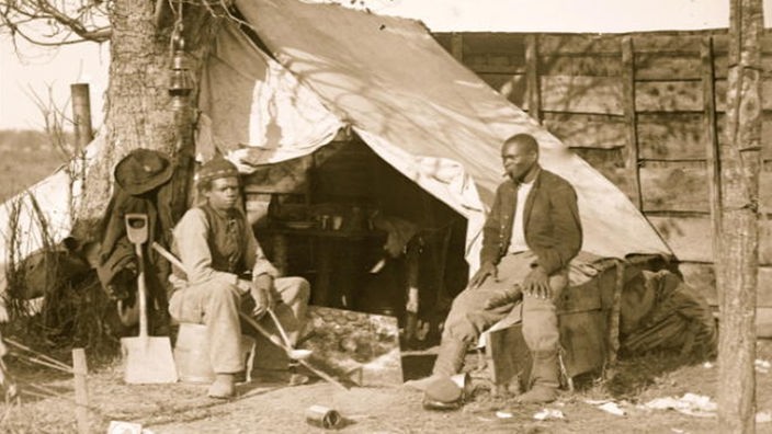 Zwei schwarze Soldaten vor einem Armeezelt.