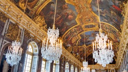 Ein großer Spiegelsaal im Schloss Versailles mit Kronleuchtern und Deckenbemalung.