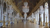 Ein großer Spiegelsaal im Schloss Versailles mit Kronleuchtern und Deckenbemalung.