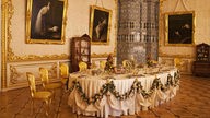 Ein opulenter Speisesaal in St. Petersburg mit gedeckter Tafel und großen Wandgemälden.