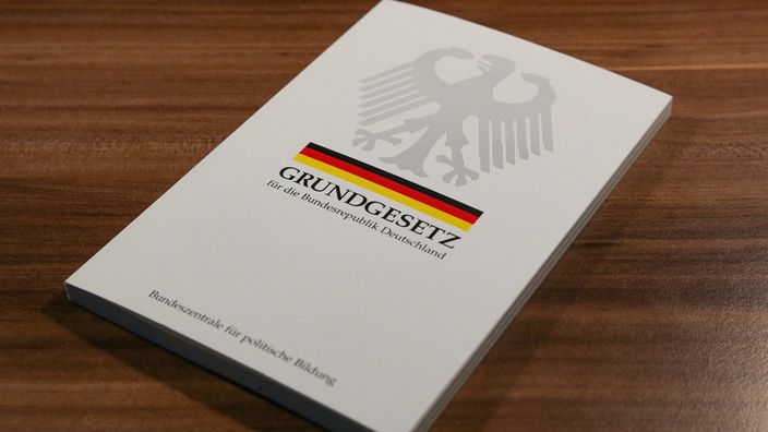 Ein Buch mit der Aufschrift „Grundgesetz“, dem deutschen Bundesadler und der deutschen Flagge liegt auf einem Tisch.