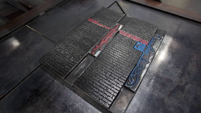Eine große metallene Druckplatte mit Lettern und Verzierungen in rot und blau.