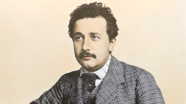 Einstein 1902 steht in seinem neuen karierten Anzug als Angestellter des Berner Patentamtes vor einem Schreibpult.