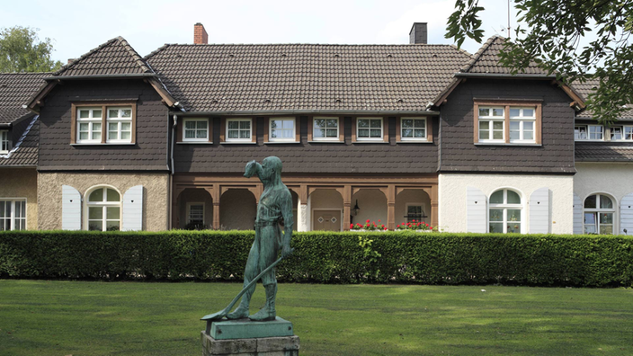 Ein Gebäude der Siedlung Altenhof in Essen, davor Rasenfläche mit der Statue eines Gießereiarbeiters.