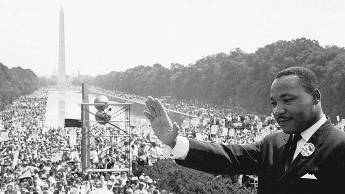 Schwarzweiß-Aufnahme: Martin Luther King grüßt eine Menschenmenge