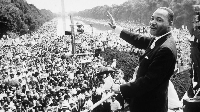 Schwarzweiß-Aufnahme: Martin Luther King grüßt in eine Menschenmenge