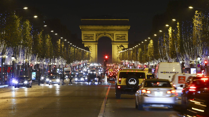 Vor dem Triumphbogen fahren Autos, die Straßenränder der Champs Elysees sind festlich beleuchtet