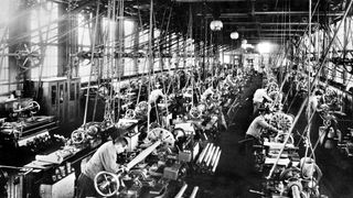 Das Schwarzweiß-Foto einer großen Fabrikhalle im 19. Jahrhundert. Dicht gedrängt steht Arbeiter an Arbeiter.