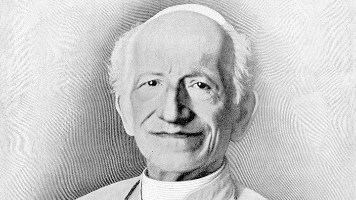 Schwarzweiß-Fotografie als Ovalausschnitt zeigt Papst Leo XIII. im Papstornat mit Kreuzkette um den Hals. Der Papst lächelt milde.