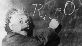 Albert Einstein steht an der Tafel und rechnet ein mathematisches Problem vor 