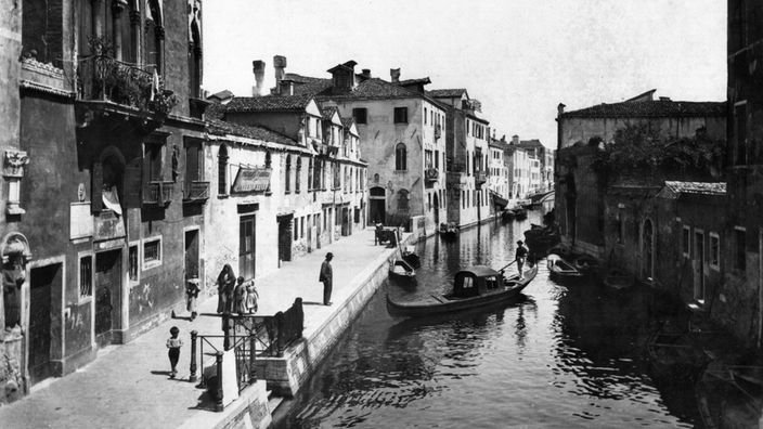 Schwarzweiß-Foto: Venezianischer Seitenkanal, links und rechts schmucklose Häuser