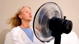 Eine ältere Dame hält einen Ventilator und kühlt sich ab