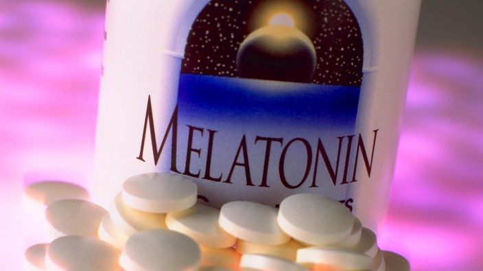 Tabletten liegen vor einem Glas mit der Aufschrift 'Melatonin'.
