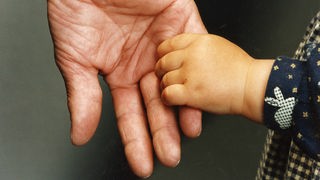Großaufnahme einer alten Hand, die die Hand eines Kleinkinds hält.
