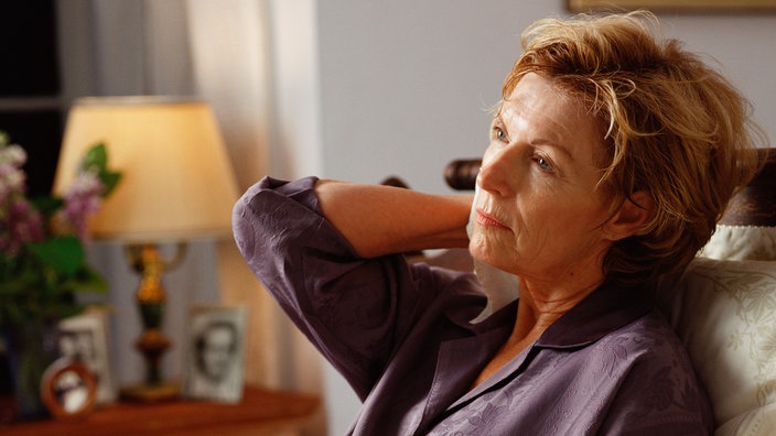 Eine ältere Dame sitzt nachdenklich auf einem Sofa | Bildquelle: Mauritius/Workbookstock Eine ältere Dame sitzt nachdenklich auf einem Sofa