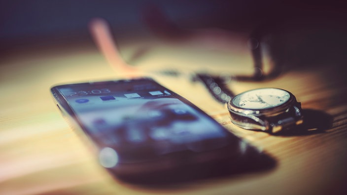Smartphone und Armbanduhr liegen neben dem Bett 