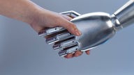 Mensch und Roboter geben sich die Hand.