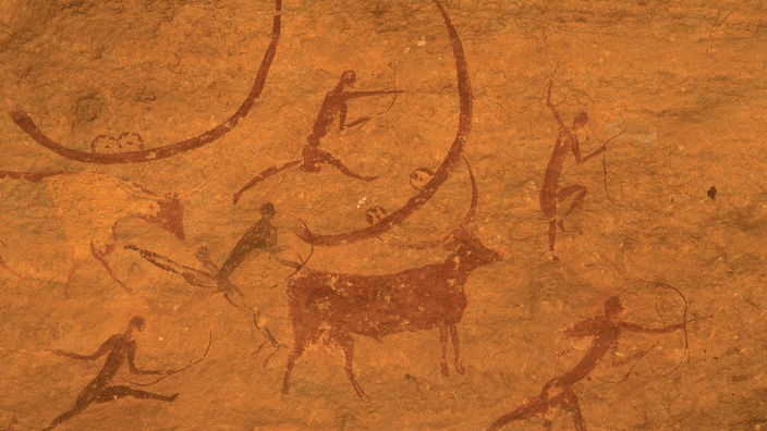 Die Fotografie einer algerischen Höhlenmalerei zeigt Menschen, die mit Pfeil und Bogen Rinder jagen.