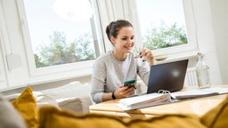 Eine Frau sitzt an einem Couchtisch und blickt auf ihren Laptop