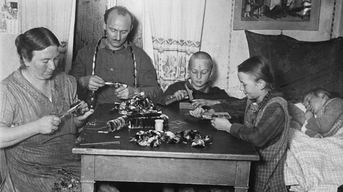 Heimarbeit um 1930: Eltern und Kinder sitzen am Küchentisch und fertigen Pfeifenreiniger