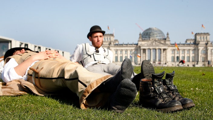 Zwei Wandergesellen liegen auf der Wiese vor dem Reichstag in Berlin | Bildquelle: picture-alliance/ dpa Zwei Wandergesellen liegen auf der Wiese vor dem Reichstag in Berlin