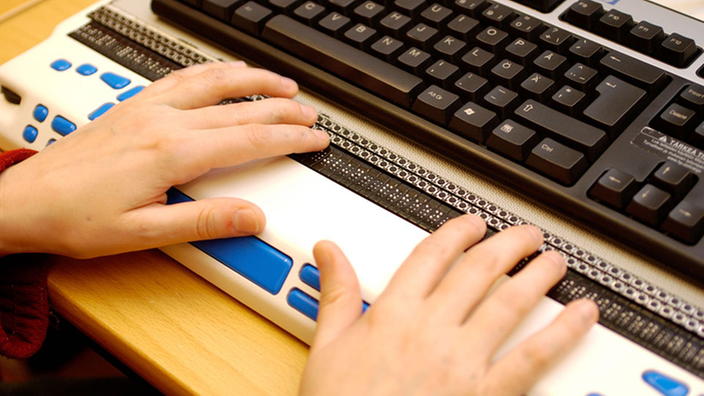 Ein Blinder schreibt auf einer Braille-Tastatur.