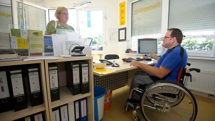 Ein Mann im Rollstuhl an seinem Arbeitsplatz an der Rezeption eines Campingplatzes