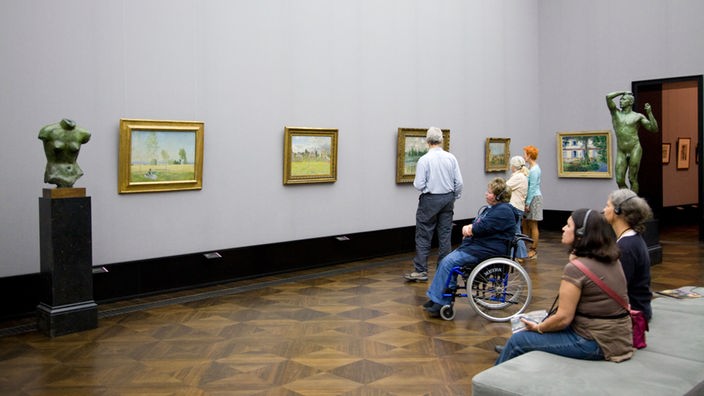 Besucher der Alten Nationalgalerie in Berlin sitzen mit Kopfhörer vor Bildern.