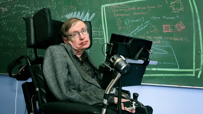 Der Physiker Stephen Hawking im Rollstuhl mit Sprachcomputer vor einer Tafel