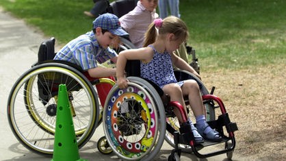 Kinder mit körperlicher Behinderung spielen miteinander im Rollstuhl.