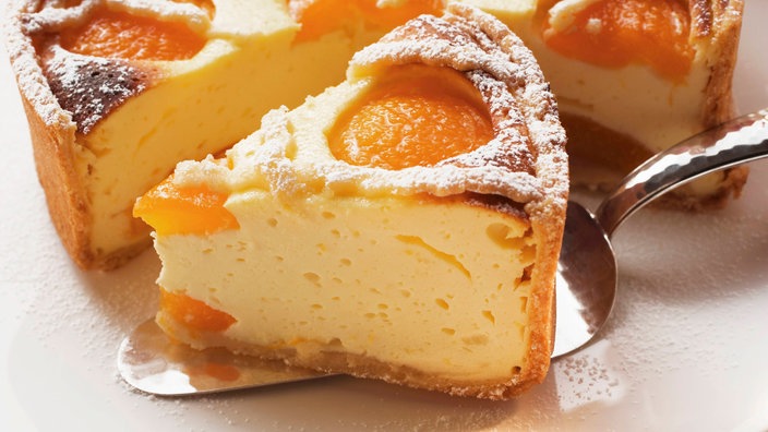 Stück Käsekuchen mit Aprikosen vor angeschnittener Torte. | Bildquelle: dpa picture alliance / Foodcollection Stück Käsekuchen mit Aprikosen vor angeschnittener Torte.