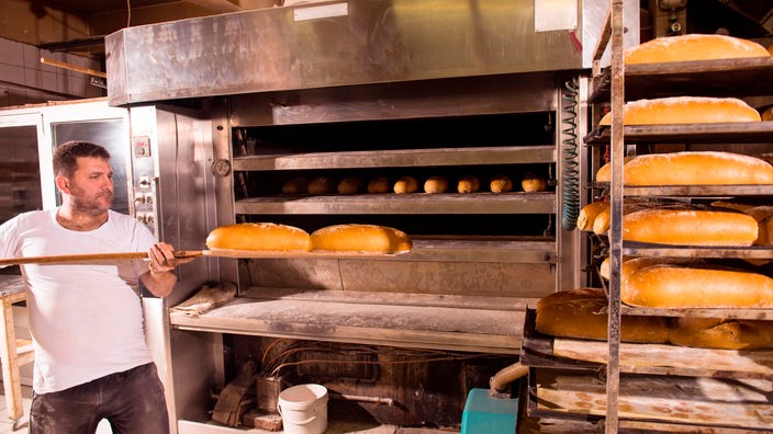 Ein Bäcker zieht fertige Brote aus einem Ofen aus Edelstahl.